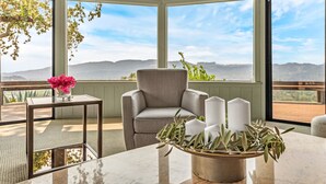 A corner seating area with a view of mountains, a cushioned chair, a small table with a vase of flowers, and a candle holder. - Escape to “Casa Paradiso” in the Napa Valley! (Calistoga)