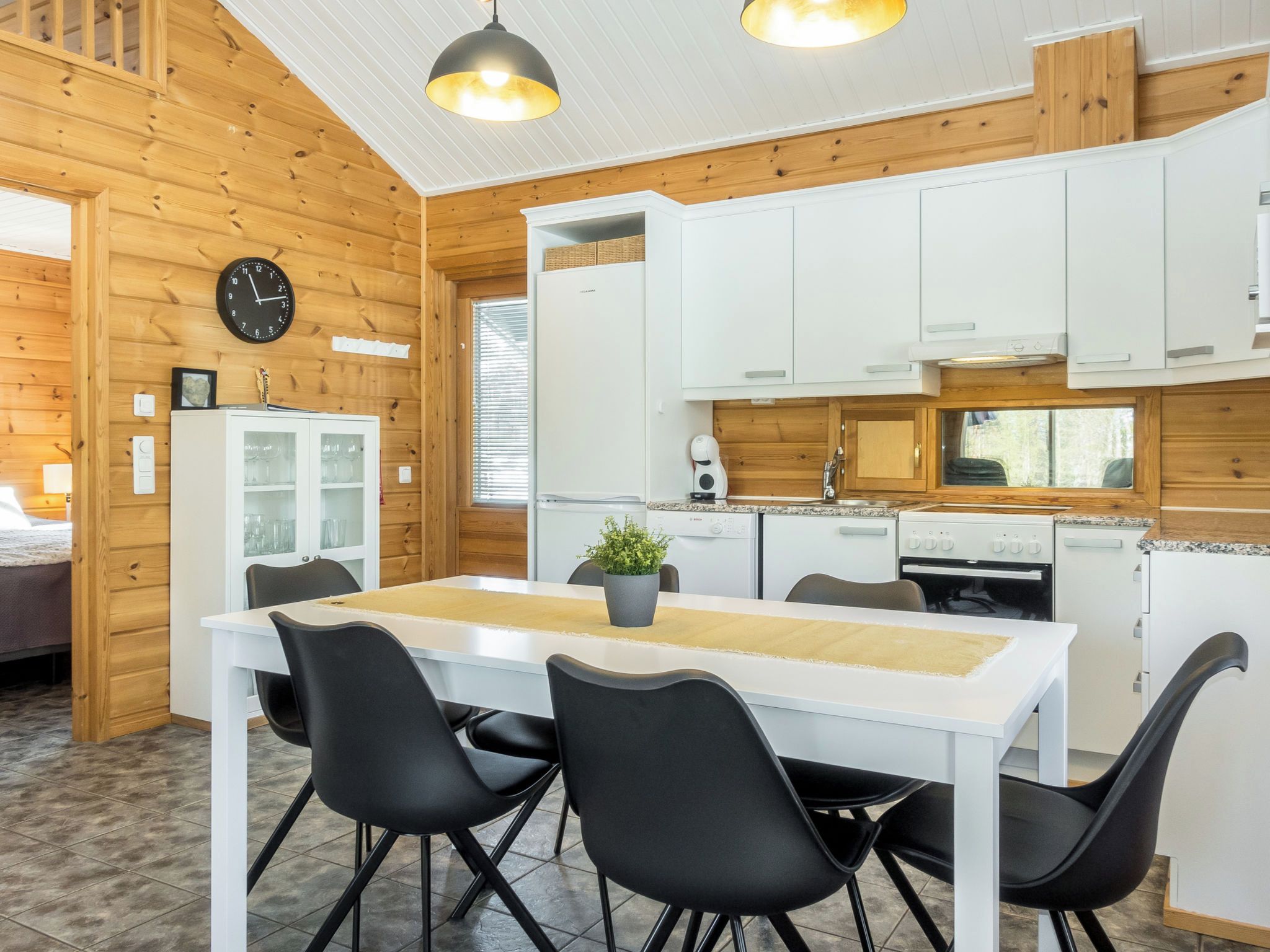 Une cuisine compacte avec des meubles blancs, un îlot central doté de chaises, une horloge et une fenêtre.
