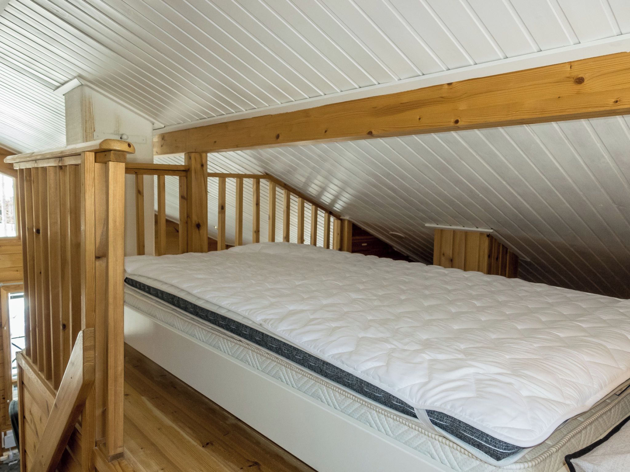 Un llit individual en una habitació d'estil loft amb bigues de fusta i un sostre inclinat.