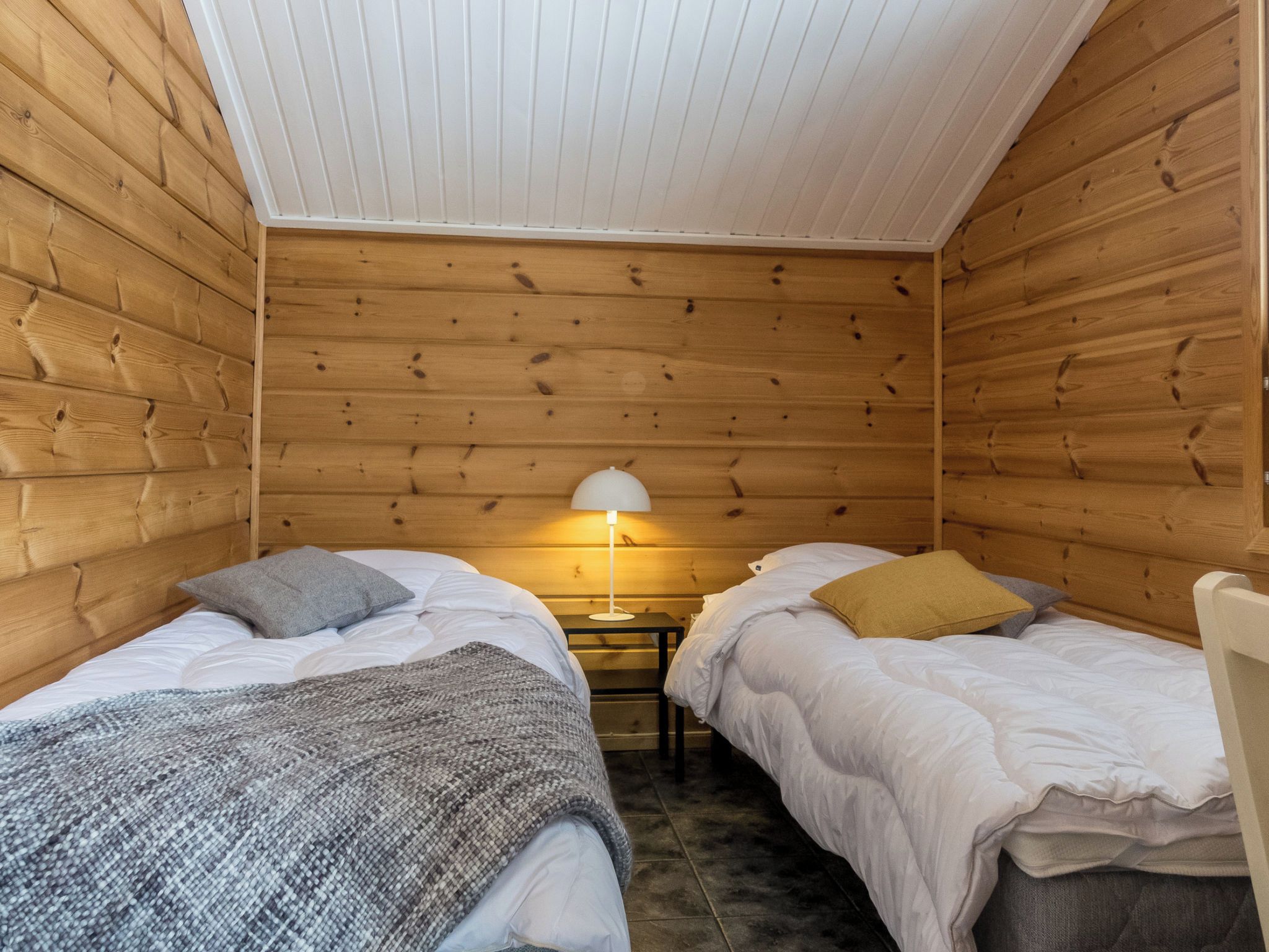 Una habitación pequeña y acogedora con dos camas, una mesita de noche y una lámpara.