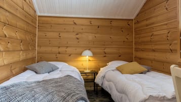 Una habitación pequeña y acogedora con dos camas, una mesita de noche y una lámpara.