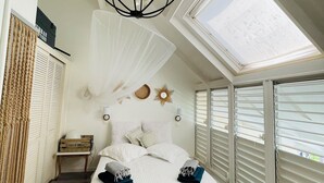 A bedroom with a bed, a chandelier, a skylight, and a wooden floor. - Blue Lagoon, Cottage feet in the water (Terre-de-Haut)