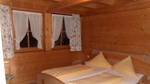 Une chambre dans une cabane en bois, avec un lit, deux fenêtres avec des rideaux et une petite table.