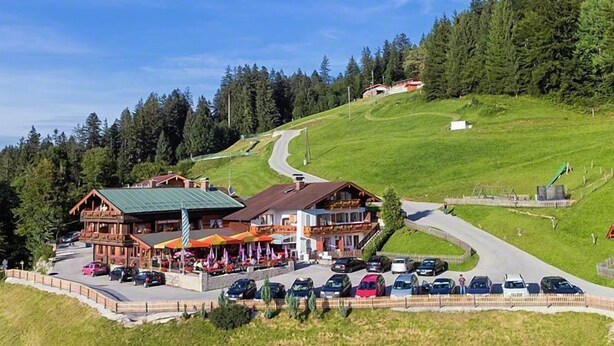 Un chalet doté d’un toit végétalisé, d’un espace de stationnement et offrant une vue sur une colline boisée.