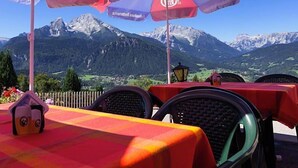 Buiten tafels met parasols, een uitzicht op de bergen en een heldere lucht.