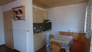 Een kleine keuken met houten kastjes, een fornuis en een eettafel met stoelen.