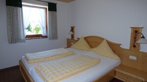 Een tweepersoonsbed met houten hoofdbord, twee nachtkastjes, een raam met gordijnen en een wandlamp.