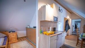 Cocina compacta con armarios de madera, microondas y una pequeña encimera. Cuenta con comedor con mesa y sillas, y una zona de descanso separada con cama.