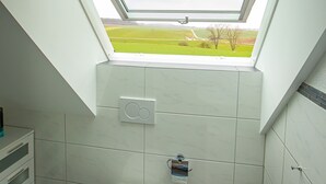 Un baño con tragaluz, inodoro, bidé y un pequeño cubo de basura.