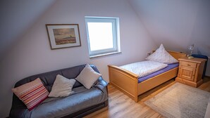 Un dormitorio con una cama de madera, un sofá gris, una mesita de noche pequeña y una ventana.