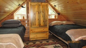 A cozy attic bedroom with two beds, a wooden wardrobe, and a window with a view.