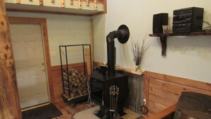 A cozy room with a wood-burning stove, a door, a bench, and a shelf with speakers.