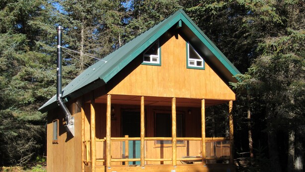 A wooden cabin with a green roof, a balcony, and a chimney.