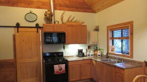 A kitchen with wooden cabinets, a stove, a microwave, a sink, and a window with blinds.