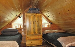 Une chambre mansardée chaleureuse, avec deux lits, une armoire en bois et une fenêtre donnant sur un beau paysage.
