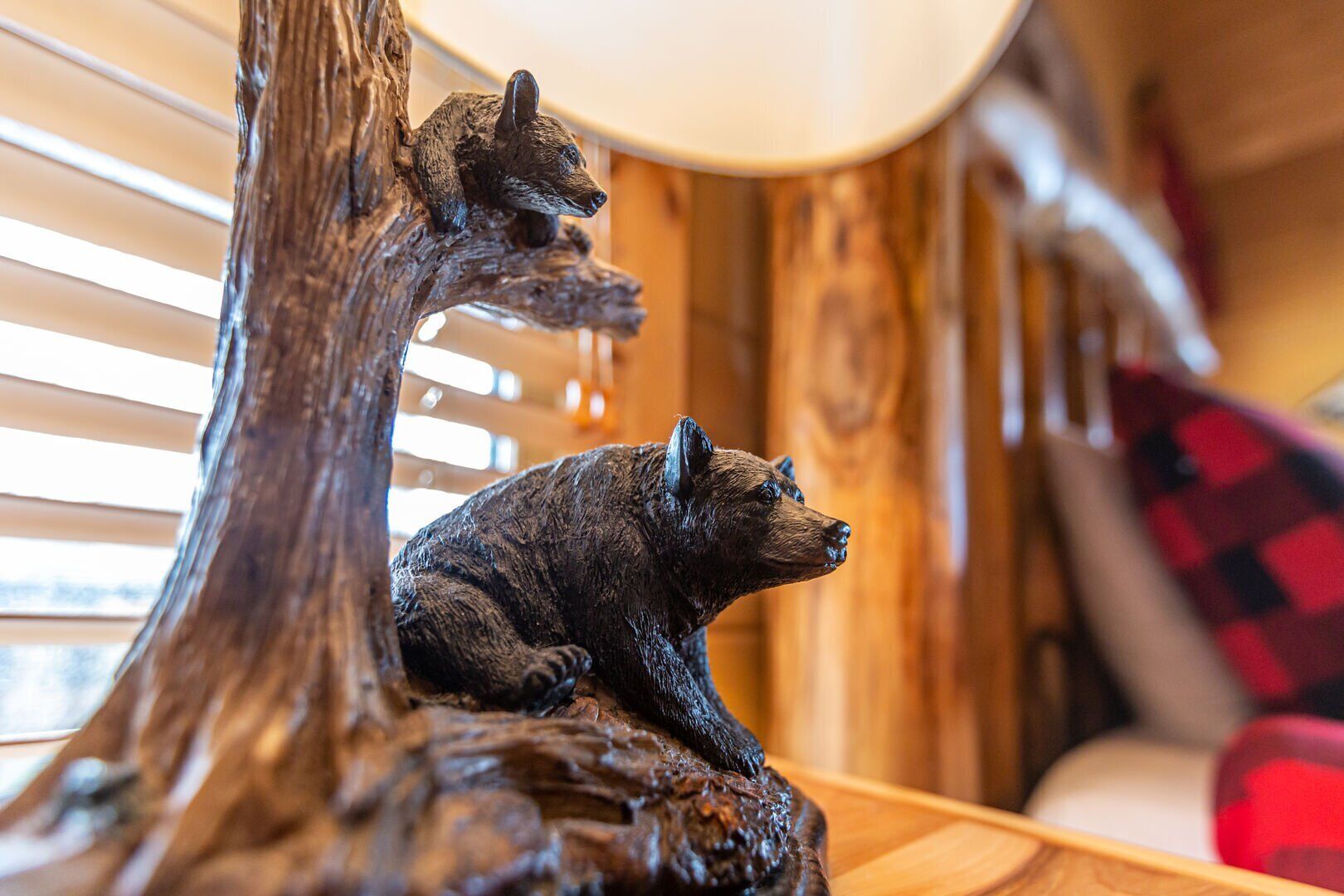 A wooden sculpture of a bear on a tree branch, a wooden table, and a red and black checkered cushion.