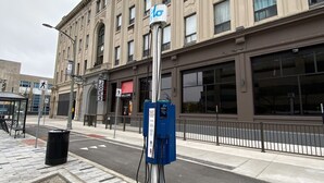 En gata med en offentlig laddstation för elfordon, ett övergångsställe och en byggnad med stora fönster och en skylt med texten ”VÄLKOMMEN”.