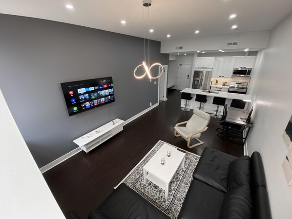 A modern living room with a flat-screen TV, a white coffee table, and a black sofa. - Fully Furnished & Renovated Historic Condo in Downtown Core (London)