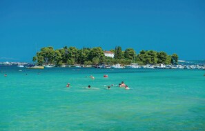 A coastal scene with clear turquoise waters, a row of boats, and a building with a red roof.