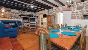 A rustic dining area with a wooden table and chairs, stone walls, and a stone fireplace. - Nice Home in Preko With Wifi and 2 Bedrooms (Preko)