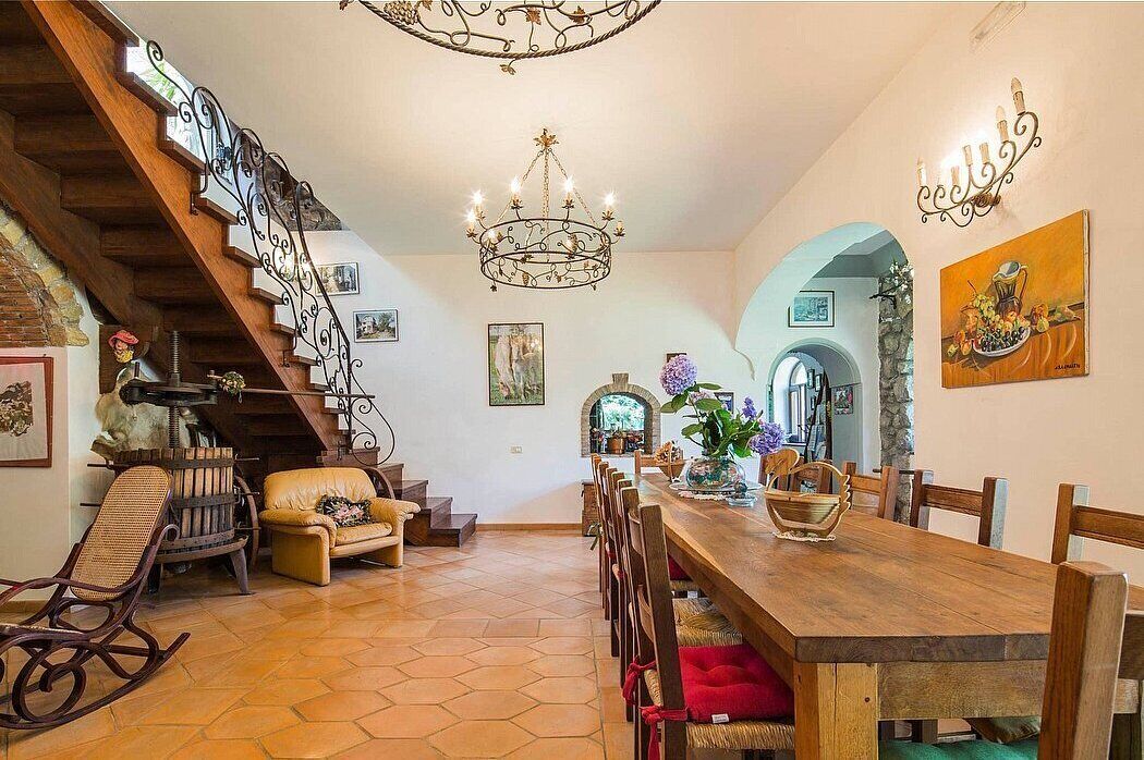 A dining area with a wooden table and chairs, a staircase with a wrought iron railing, and a chandelier.