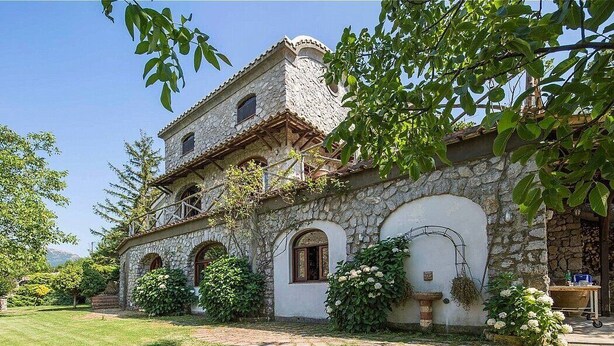 Ein Gebäude aus Stein mit rustikaler Fassade, mehreren Bögen und einem Gartenbereich mit Grünpflanzen und Blumen.