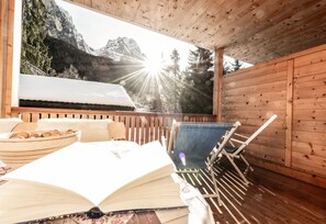 A wooden cabin with a view of mountains, a dining table with a bowl of cookies, and a chair. - Apartment "Bergfrieden 2 A" with Mountain View, Pool, Wi-Fi, Terrace & Garden (Seis am Schlern BZ)