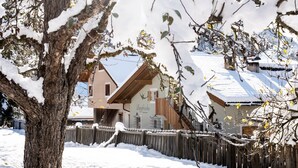 Ett snötäckt bostadsområde med ett trästaket, ett hus med ett sluttande tak och ett träd i förgrunden.