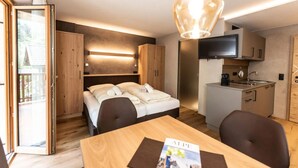 Ett kompakt hotellrum med en säng, ett matbord, en TV och ett litet kök.
