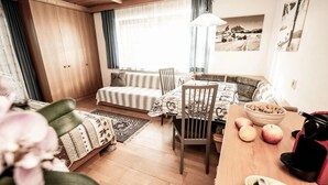 A cozy room with a wooden ceiling, a sofa with patterned cushions, a dining table with chairs, a fruit bowl, and a kettle. - Apartment "Bergfrieden 2 B" with Mountain View, Pool, Wi-Fi, Terrace & Garden (Seis am Schlern BZ)