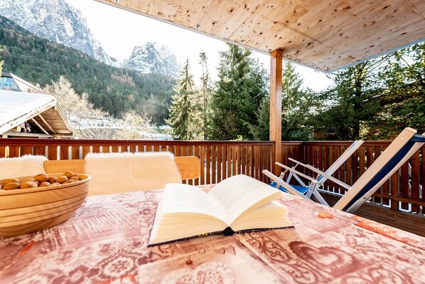 A wooden deck with a table, an open book, and a bowl of nuts.