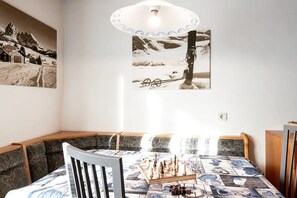 A room with a bed, a chair, a table with chess pieces, and two wall-mounted pictures.