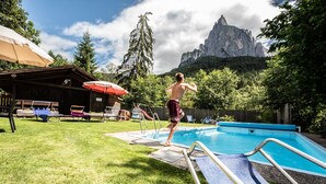 A swimming pool with a wooden deck, lounge chairs, and a mountain backdrop. - Apartment "Bergfrieden 2 B" with Mountain View, Pool, Wi-Fi, Terrace & Garden (Seis am Schlern BZ)