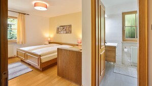 Een slaapkamer met een bed, nachtlampjes, een raam en uitzicht op de badkamer.