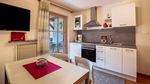 Een kleine keuken met een eethoek, een tv aan de muur en een raam met gordijnen.