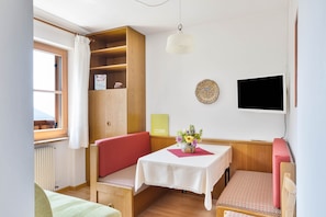 Una habitación con un banco de madera, una mesa con un jarrón de flores, un televisor y una ventana con cortinas.