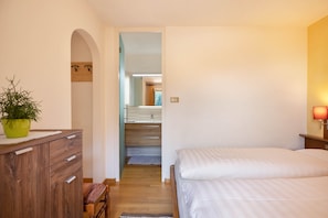 Un dormitorio con cama, cómoda de madera, planta en maceta y un pasillo que conduce a un baño.