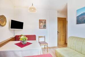 A room with a bed, a table with a vase of flowers, a television, a painting, and a door.