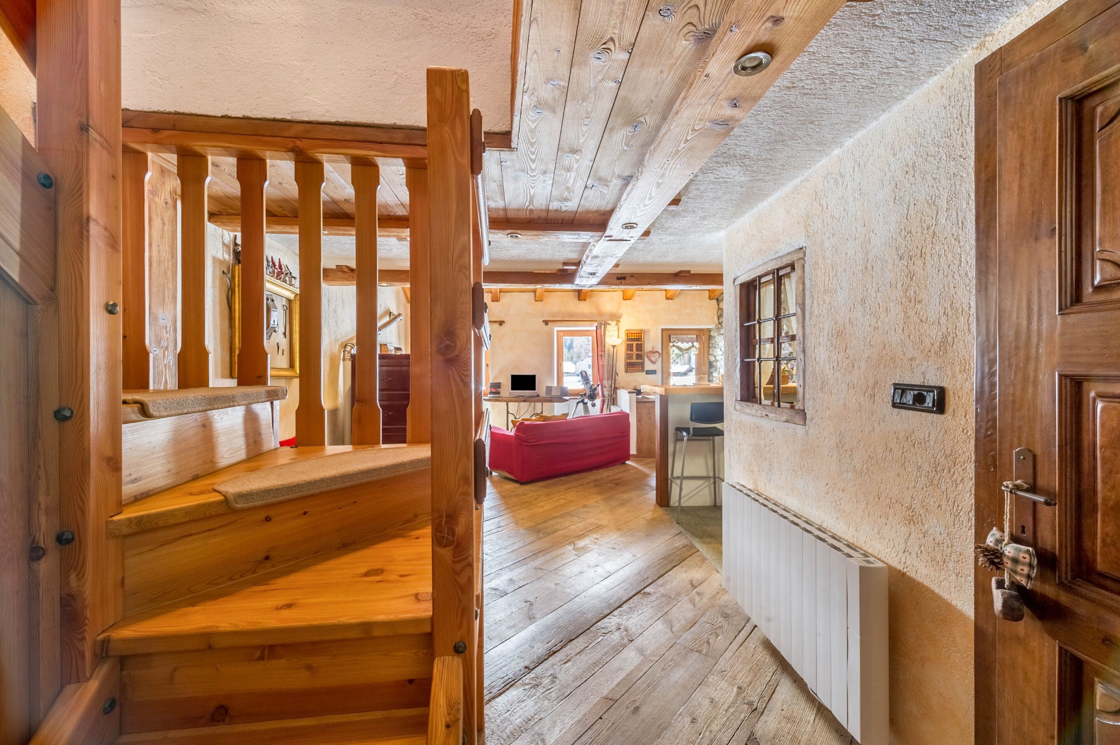 Eine Holztreppe führt zu einem Raum mit einem roten Sofa, einem Heizkörper und einer Holztür.