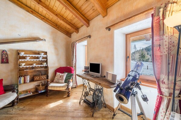 A cozy room with a wooden ceiling, a telescope, a TV, a bookshelf, and a window with a view of trees. - Holiday Home 'Arpy An' with Mountain View, Balcony and Wi-Fi (Morgex)