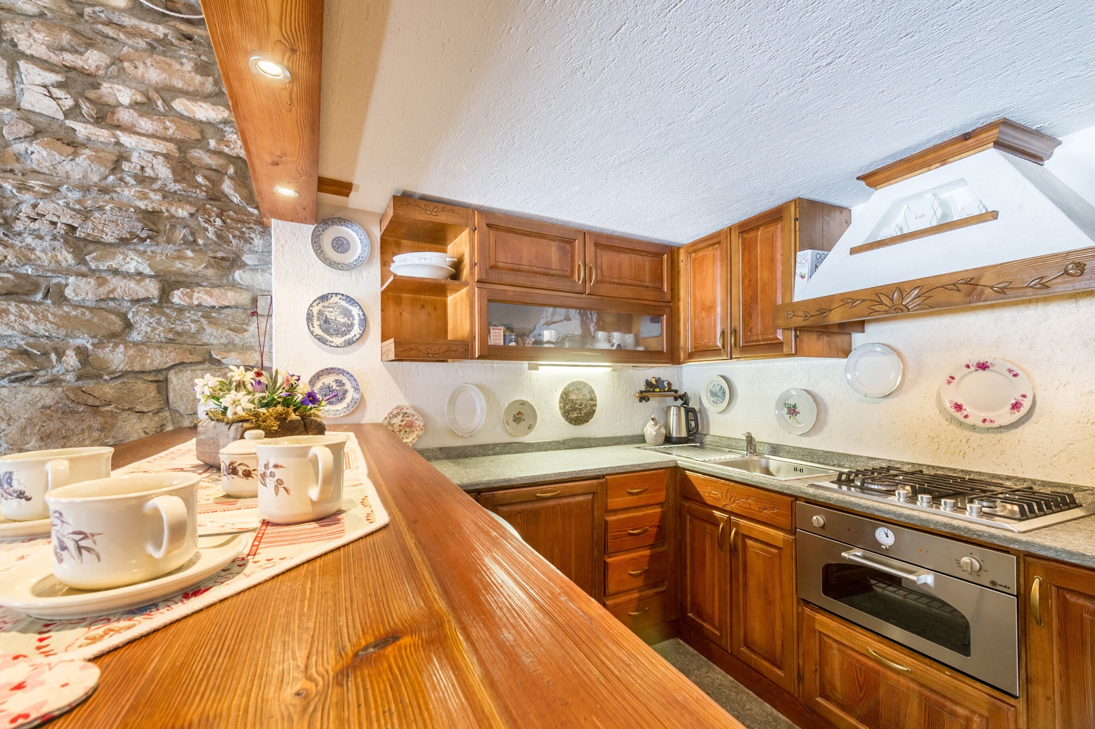 A kitchen with wooden cabinets, a stone wall, and various dishes on the wall.