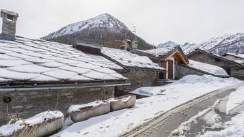 A snow-covered village with stone buildings, a road, and mountains in the background.