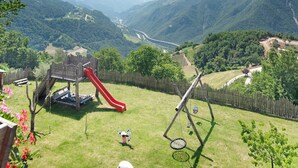 A playground with a slide and swing set, surrounded by a wooden fence and lush greenery. - Apartment "Stinerhof - Panoramablick" with Mountain View, Balcony & Garden (Völs am Schlern)