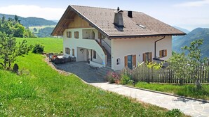A two-story house with a stone staircase, a wooden fence, and a view of the surrounding landscape. - Apartment "Stinerhof - Panoramablick" with Mountain View, Balcony & Garden (Völs am Schlern)