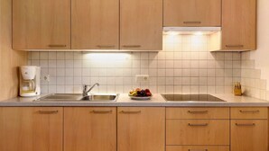 A kitchen with wooden cabinets, a double sink, a coffee maker, and a fruit bowl. - Apartment "Stinerhof - Panoramablick" with Mountain View, Balcony & Garden (Völs am Schlern)