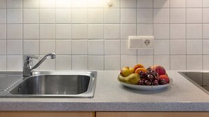A kitchen with a stainless steel sink, a bowl of fruit on the counter, and white tiled walls. - Apartment "Stinerhof - Panoramablick" with Mountain View, Balcony & Garden (Völs am Schlern)