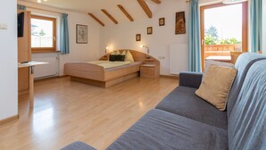 A bedroom with a wooden bed, a grey sofa, a desk, and a window with curtains. - Apartment "Stinerhof - Schlernblick" with Mountain View, Wi-Fi, Balcony & Garden (Völs am Schlern)