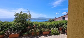 Un balcón con plantas en macetas y vistas al mar y a las montañas.