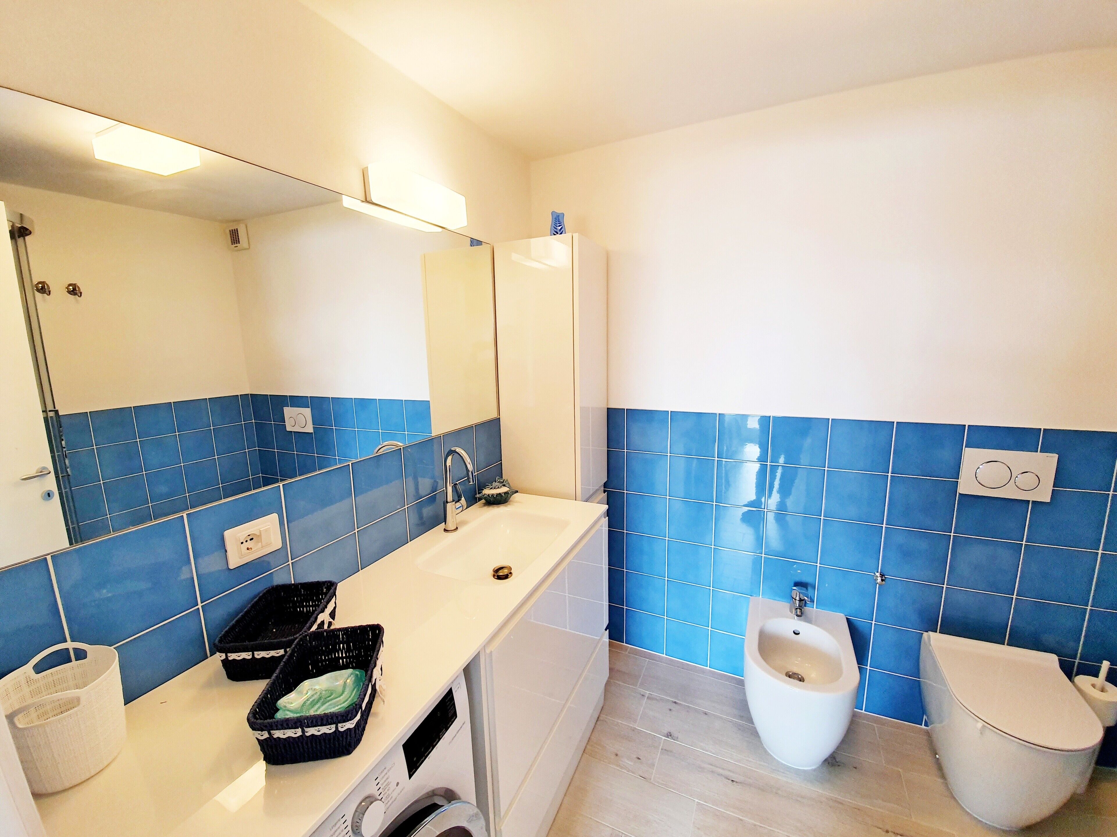 A bathroom with a sink, mirror, bidet, toilet, and a washing machine.