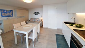 Een moderne keuken met witte kasten, een eettafel met stoelen, een bank en een klein keukeneiland met een spoelbak.